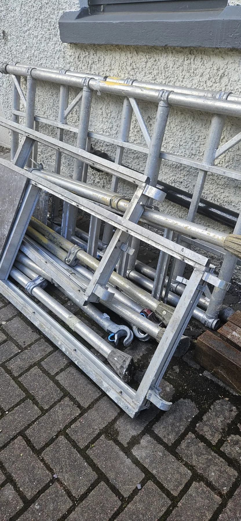 Aluminium scaffold tower sections leaning against a wall on block paving