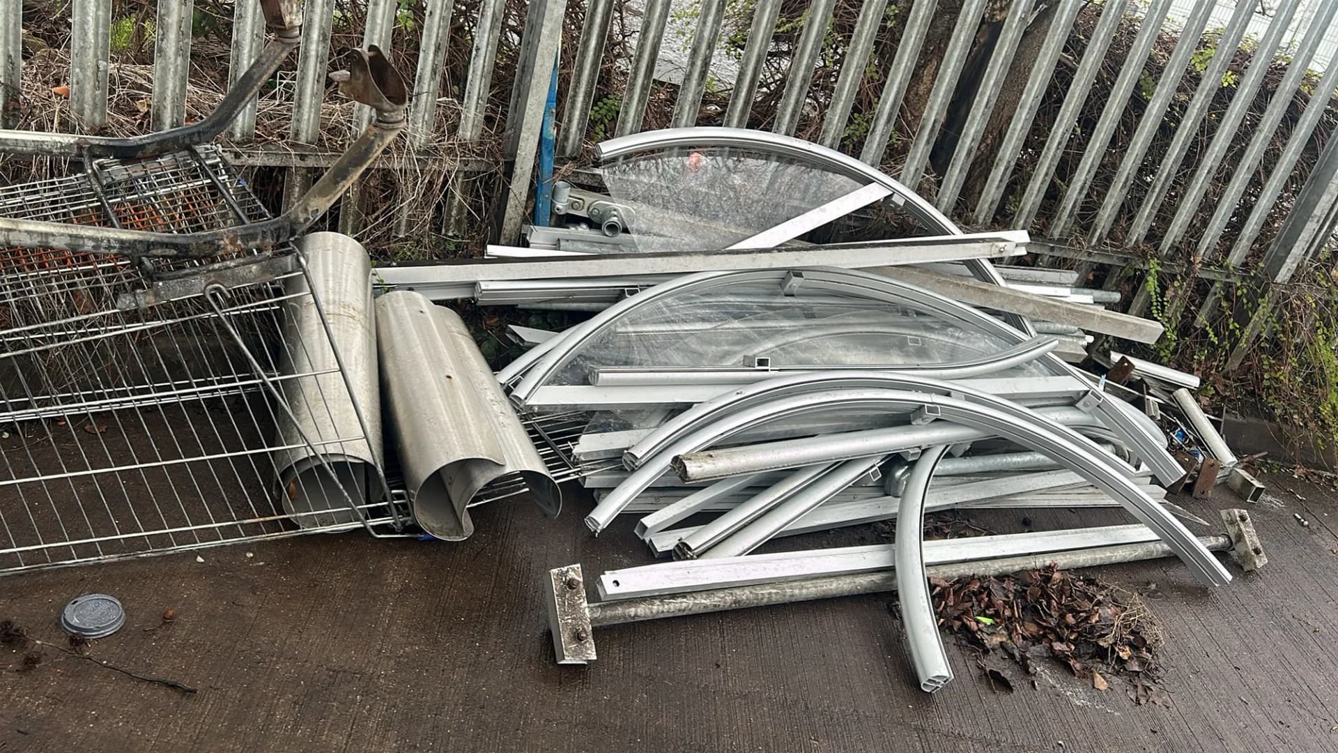 Curved aluminium sections, a cage trolley and steel posts beside a palisade fence