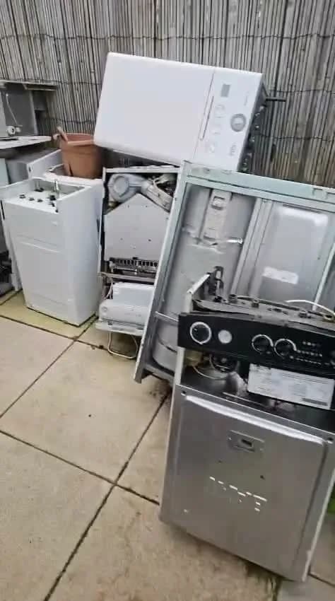 Washing machines, a tumble dryer and other white goods stacked against a house wall ready for collection
