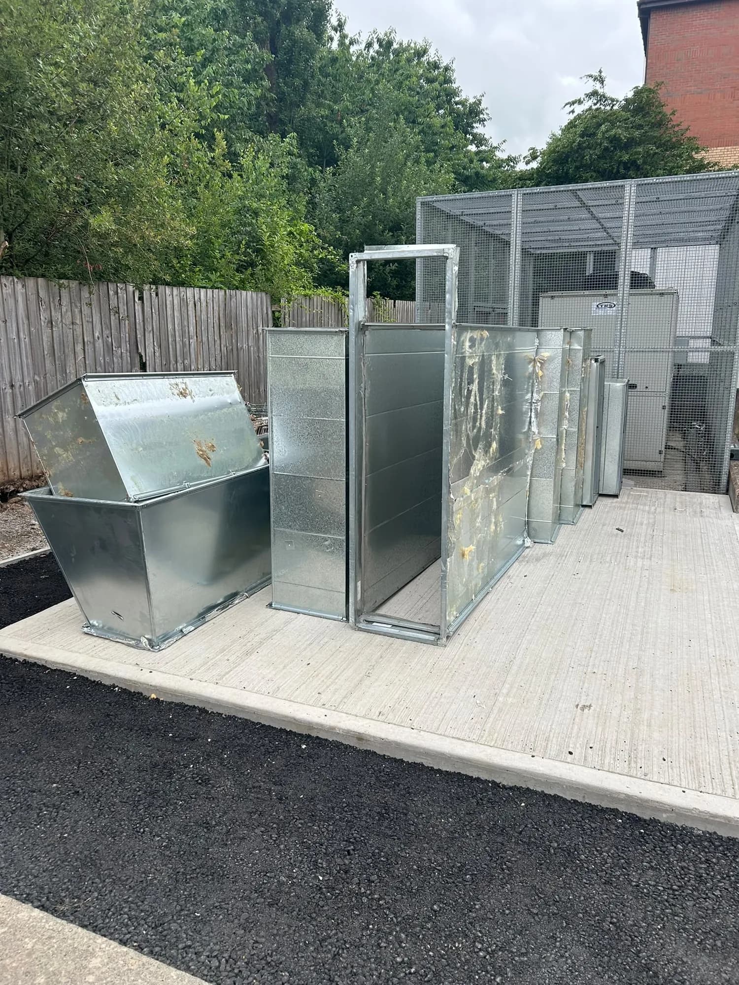 Galvanised ductwork and ventilation units on a concrete pad inside a fenced compound