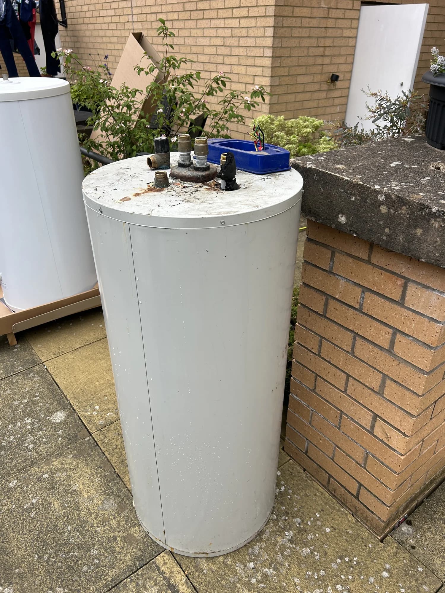 White hot water cylinder standing on paving outside a brick house