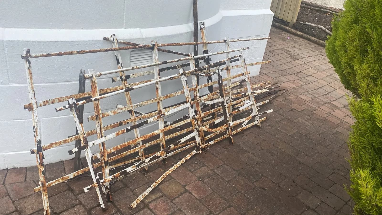 Rusted iron gate panels leaning against a white wall on block paving