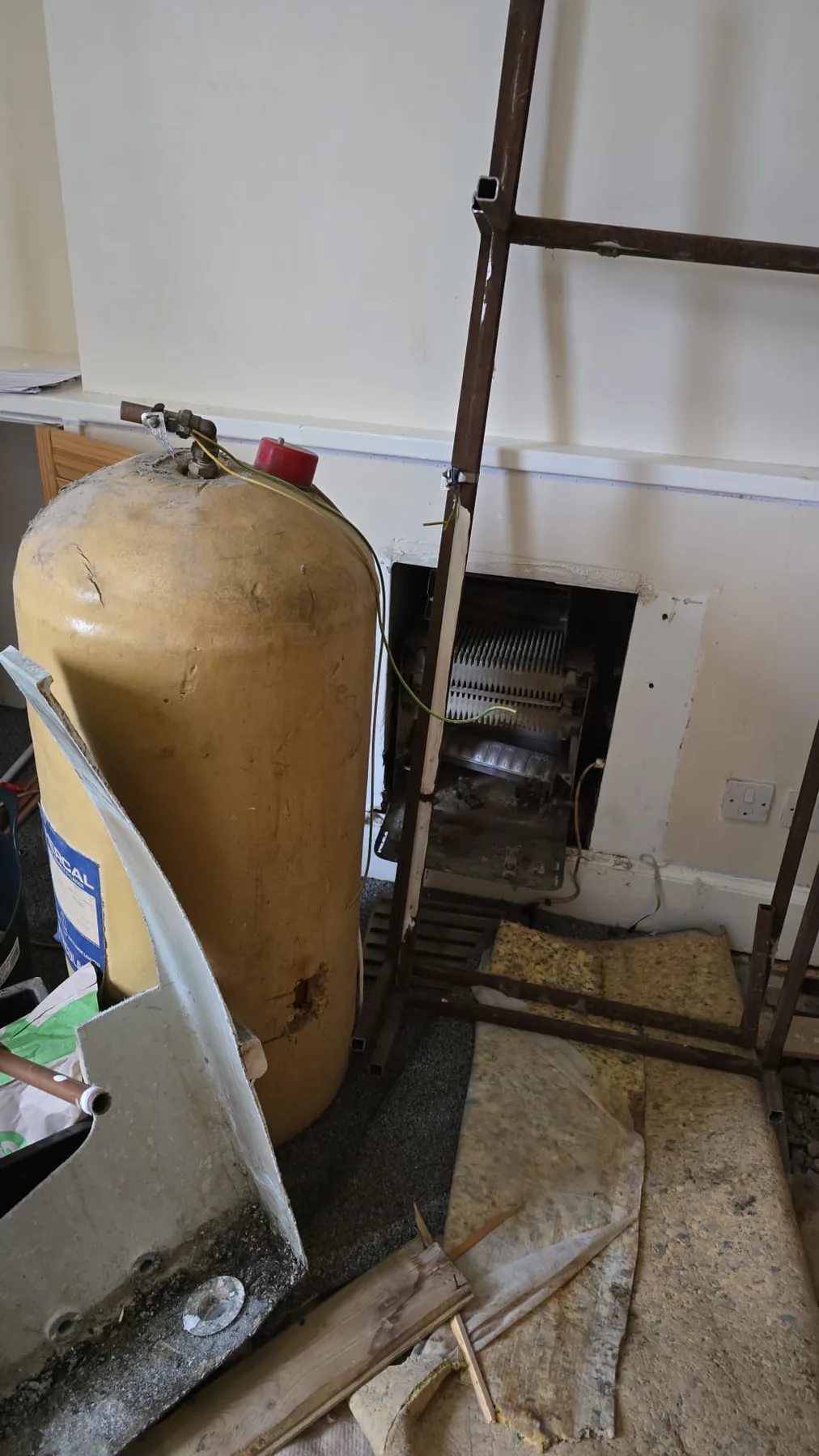 Old lagged cylinder and the empty cavity where a back boiler has been removed, in a stripped room