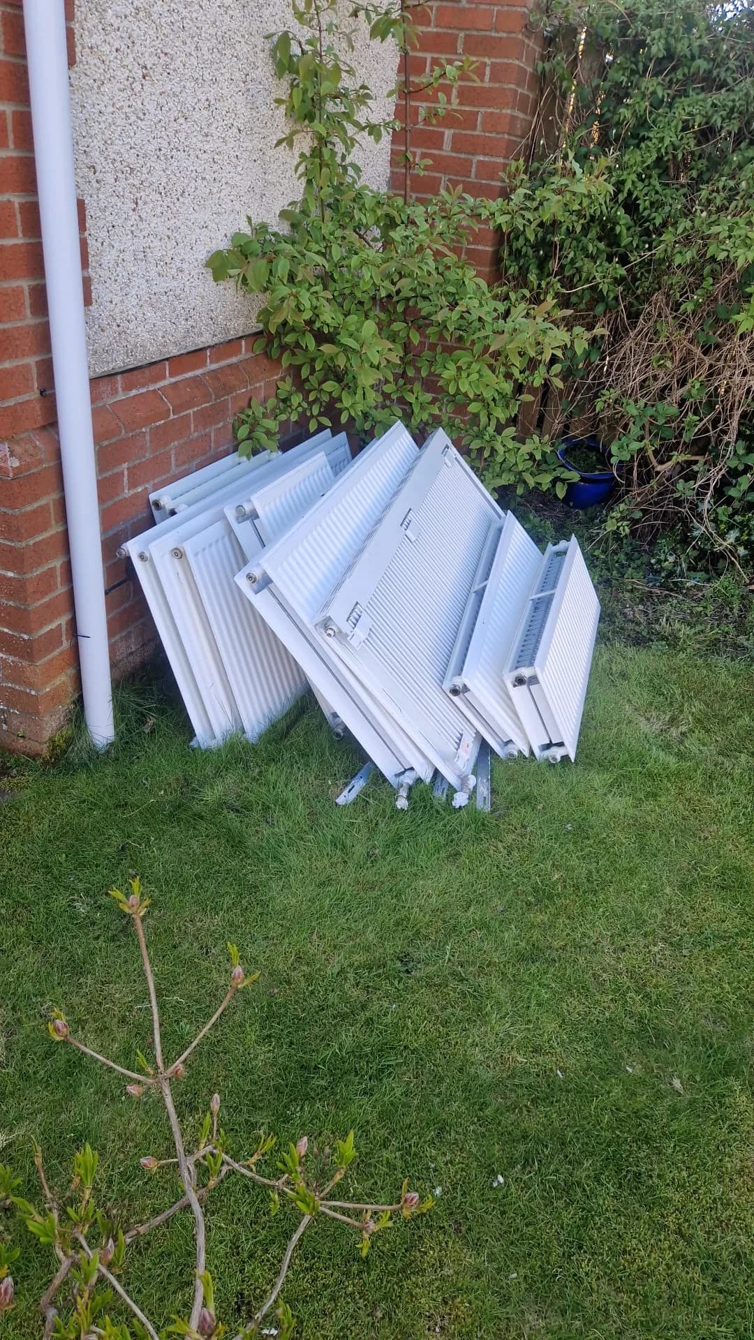 Panel radiators stacked against the brick wall of a house on a lawn