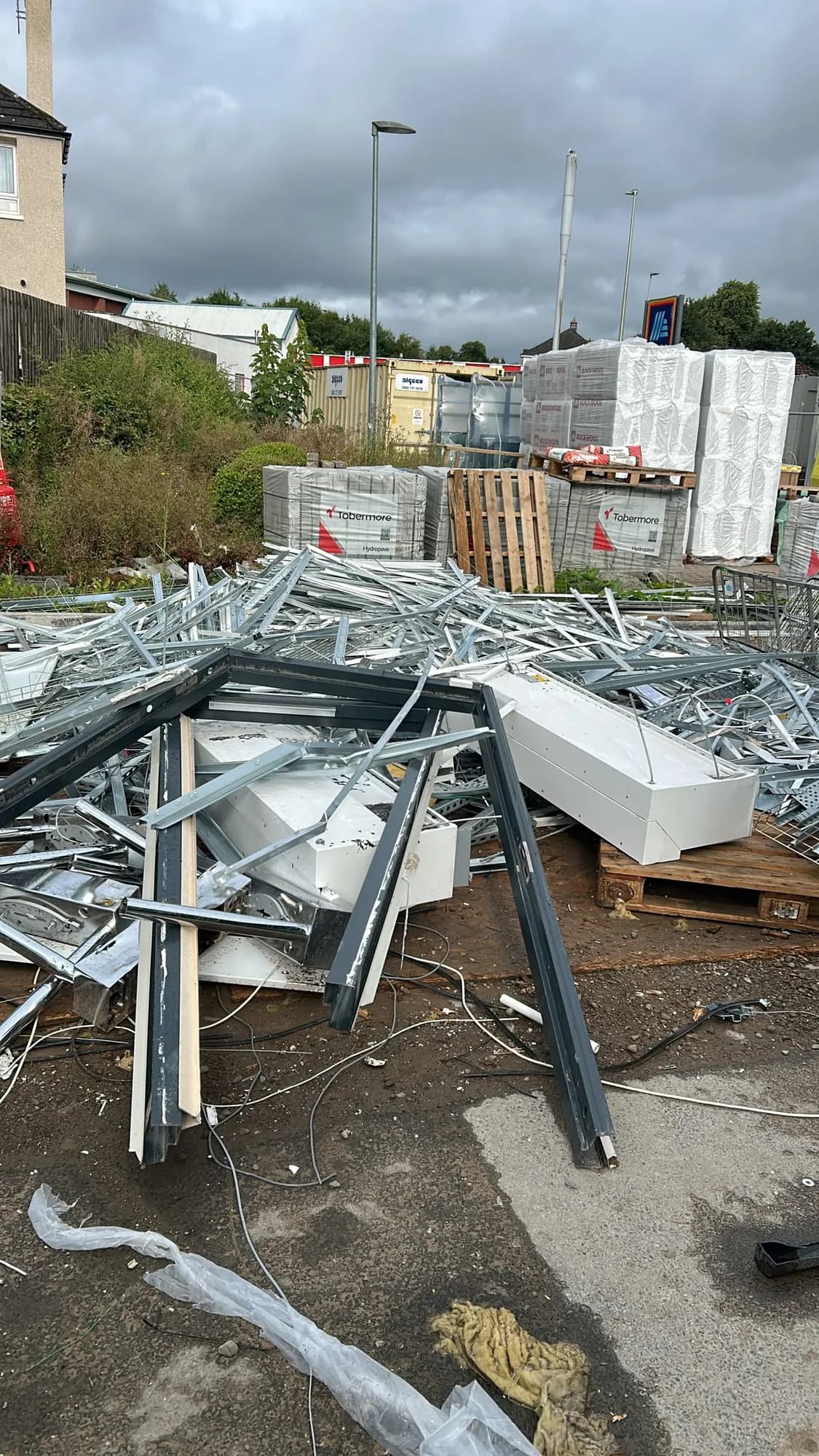 Pile of aluminium and steel shopfront sections in a builders' yard with pallets of blocks behind