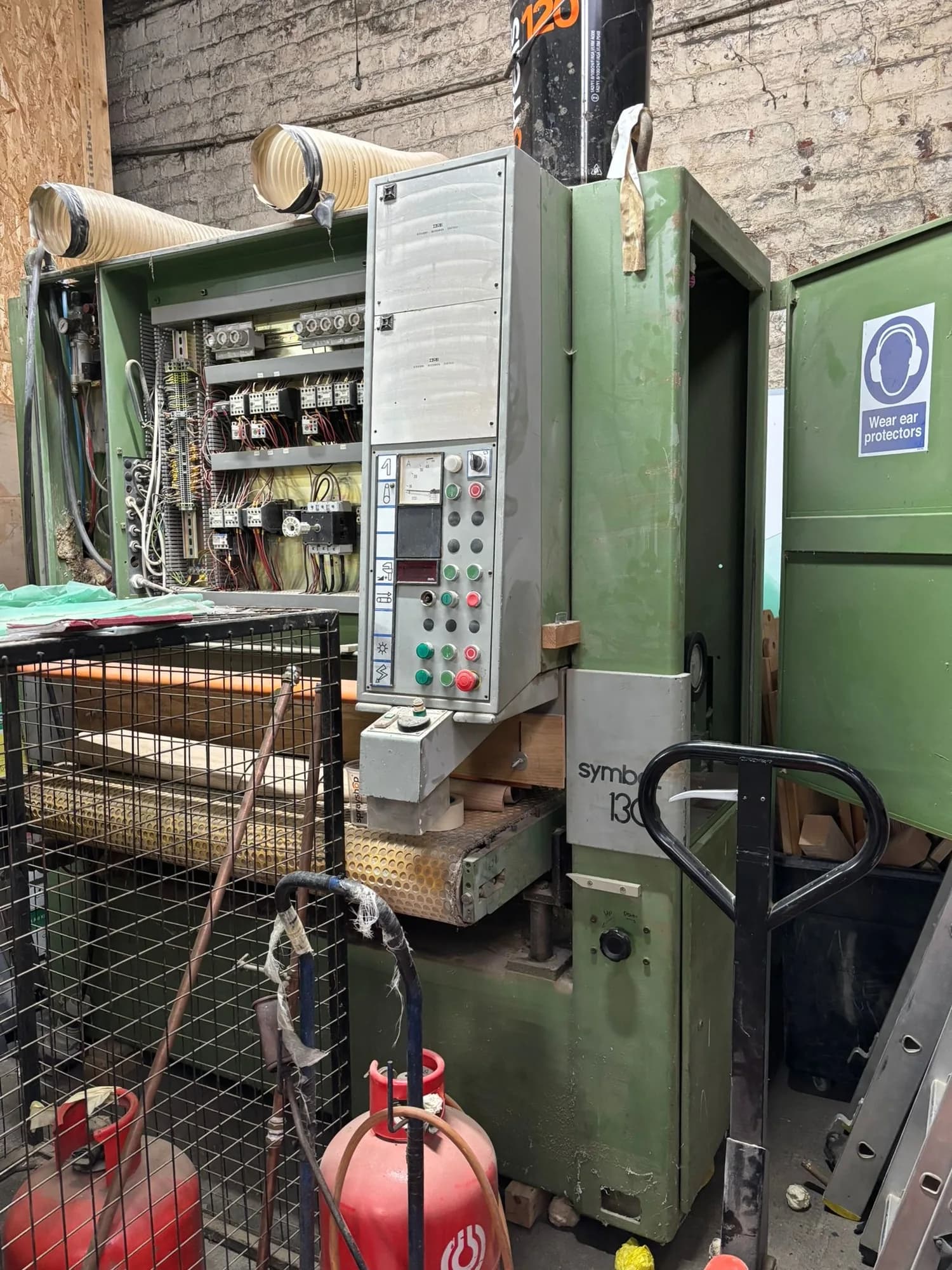 Green industrial woodworking machine with its control panel open inside a workshop
